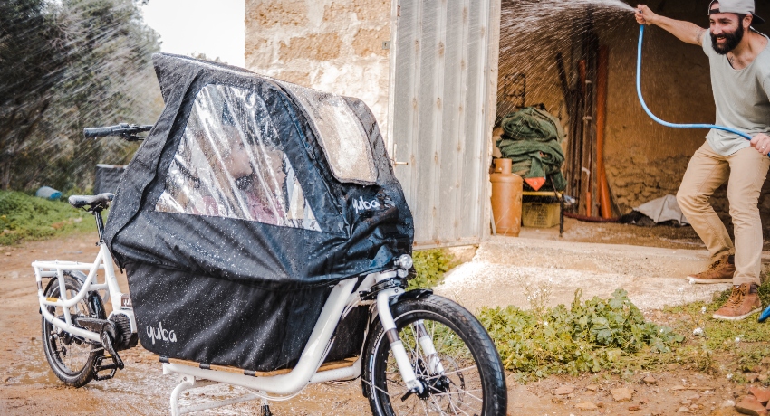Vélo cargo avec des enfants protégés par la tente de pluie