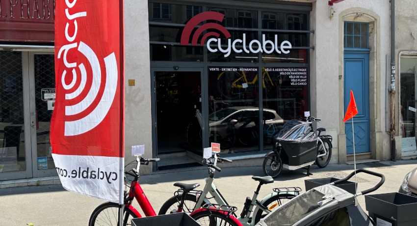 La devanture du nouveau magasin Cyclable Nancy avec un bimoteur et un VAE équipé d'une remorque enfant exposé en extérieur.