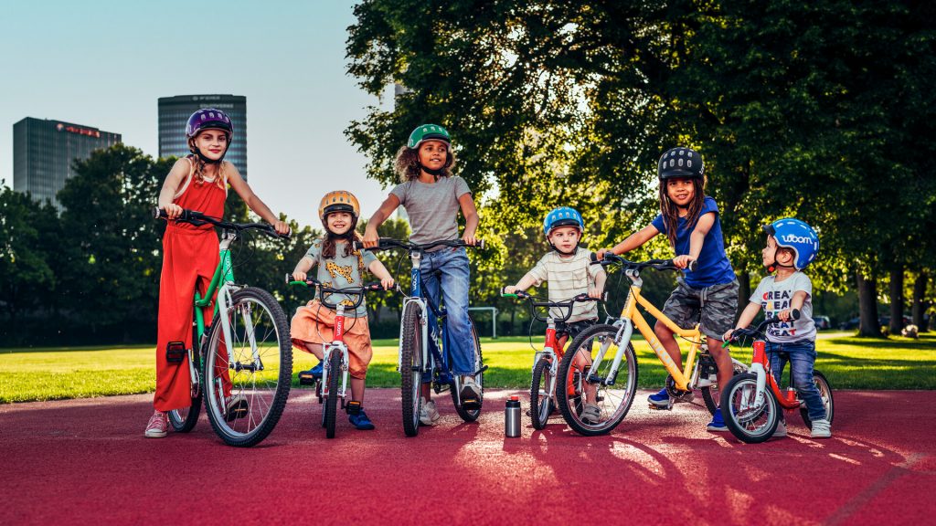 Six enfants d'âges différents dans un parc au guidon des différents vélos woom de la gamme Original, de la draisienne au 26 pouces.