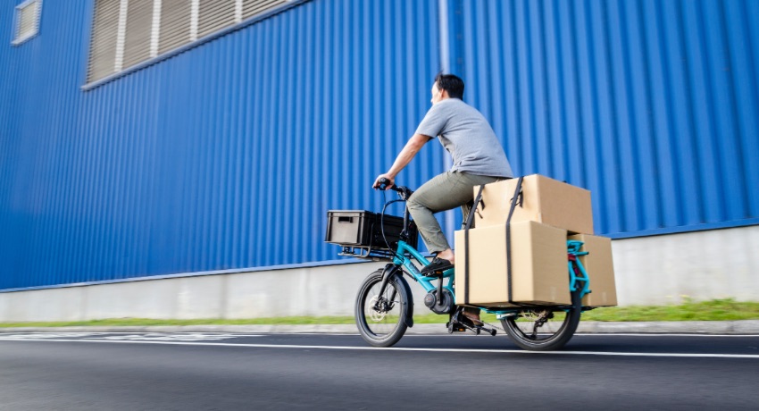 Un homme au guidon d'un longtail Tern GSD chargé de volumineux cartons.