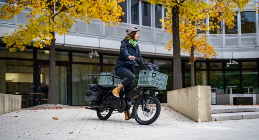 Une femme au guidon d'un vélo longtail Moustache Lundi 20 équipé de plusieurs paniers et sacoches.