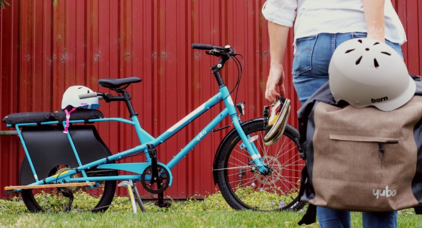 Une femme se dirige vers un vélo longtail musculaire Yuba Kombi stationné contre un conteneur.