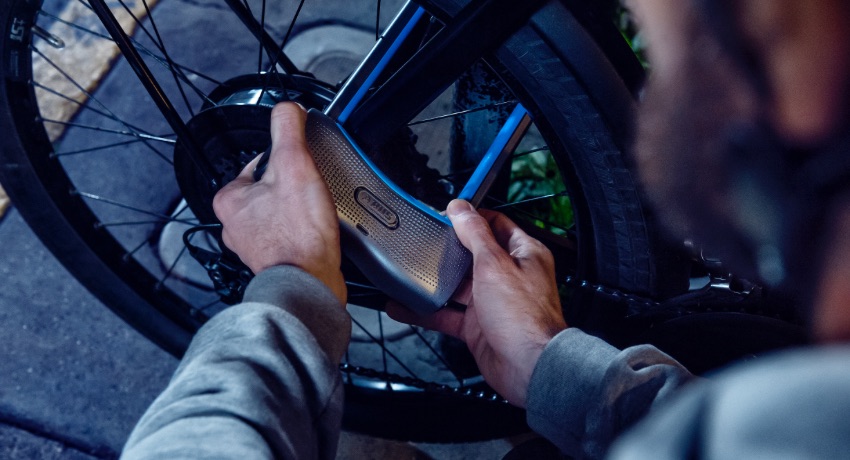 Zoom sur deux mains en train d'attacher un antivol Abus en U autour du cadre et de la roue arrière d'un VAE.