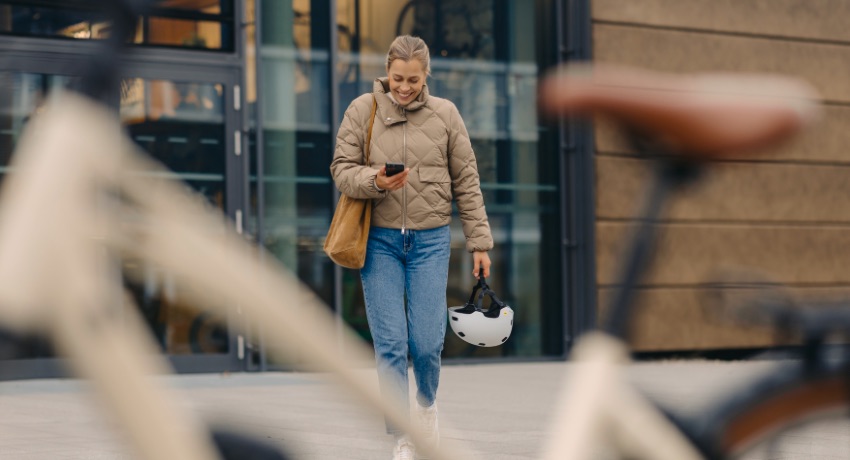 Une femme casque à la main se dirige vers son VAE tout en déverrouillant sur son smartphone son antivol numérique.