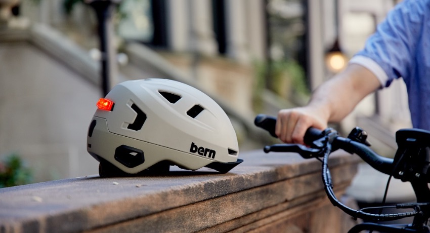 Un casque Bern blanc posé sur un muret à côté d'un guidon de vélo sur lequel une main est posée.