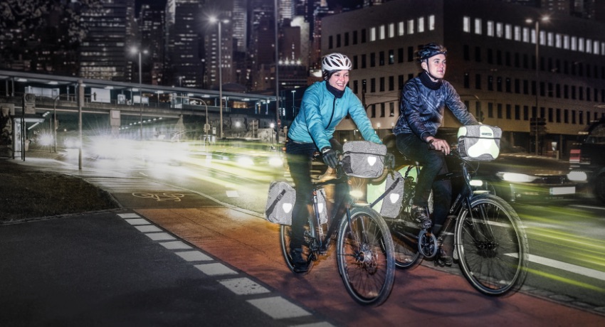 Deux cyclistes roulent de nuit sur une bande cyclable avec leurs feux allumés.