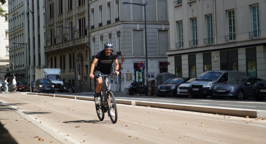 Un cycliste sur un VAE pédale en danseuse sur une piste cyclable aménagée à l'écart de la circulation automobile.