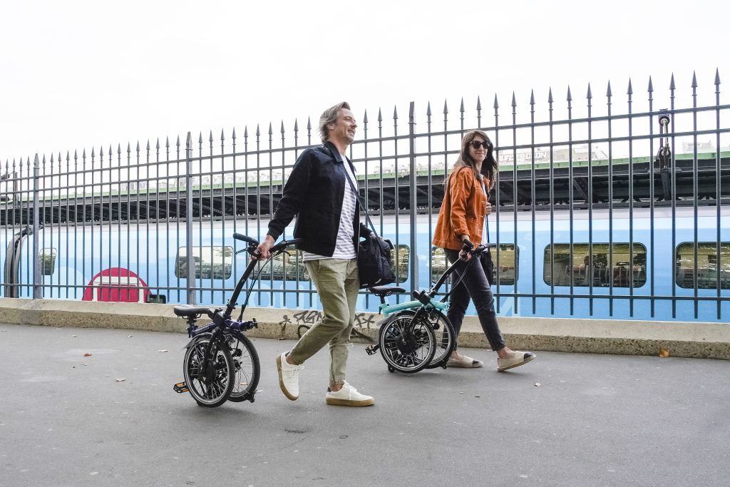 Une femme et un homme marchent sur un quai de gare en tirant leur Brompton électrique comme une valise. 