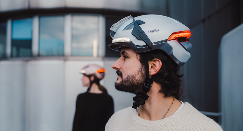 Un homme de profil pose au premier plan avec le casque Abus Hyp-E équipé d'une visière translucide. Au second plan, une femme pose dans la même attitude.