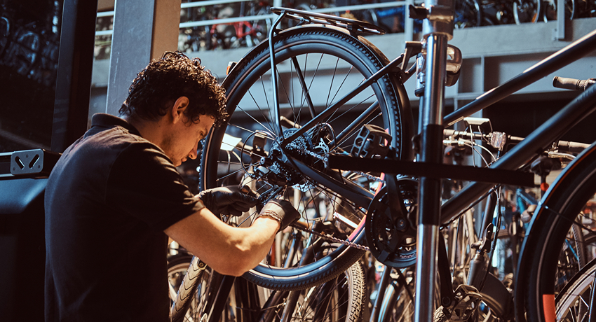 Un jeune homme révise la transmission d'un vélo installé sur un pied d'atelier.