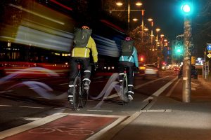 Deux cyclistes de dos pédale sur une bande cyclable urbaine de nuit avec leur éclairage et équipements d'hiver.