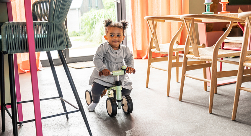 Une petite fille se déplace dans le salon familial au guidon d'un porteur Puky.