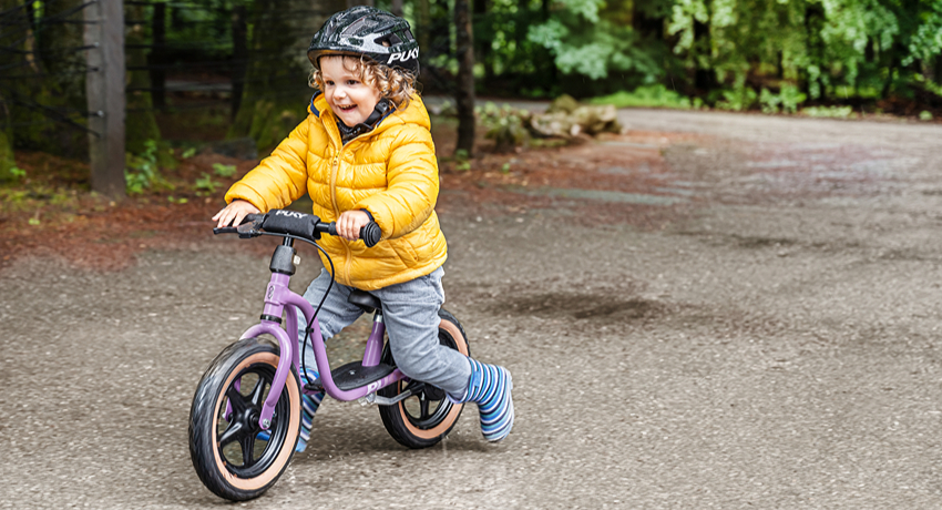 Un petit garçon fonce au guidon de sa draisienne Puky entre les flaques d'une petite route forestière.