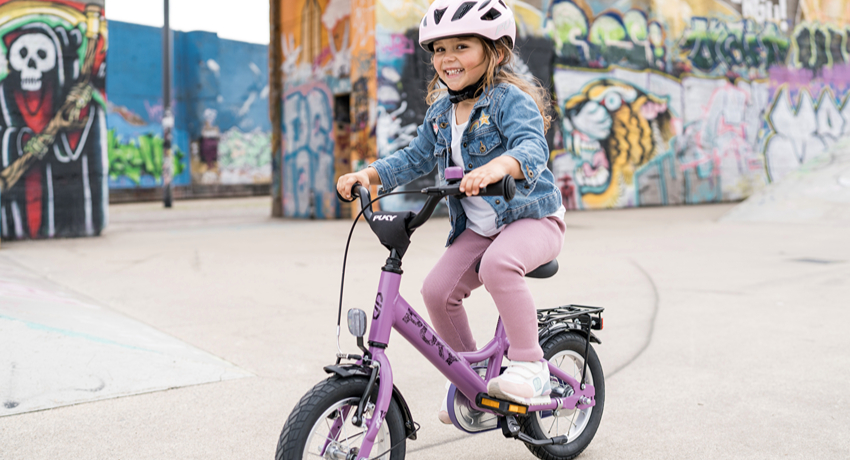 Une petite fille roule sur une esplanade urbaine au guidon d'un vélo Puky Youke.