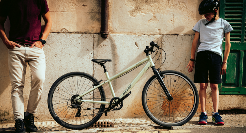 Un vélo Puky LS-Pro 26 pouces appuyé à un mur entre un jeune adolescent et son père.