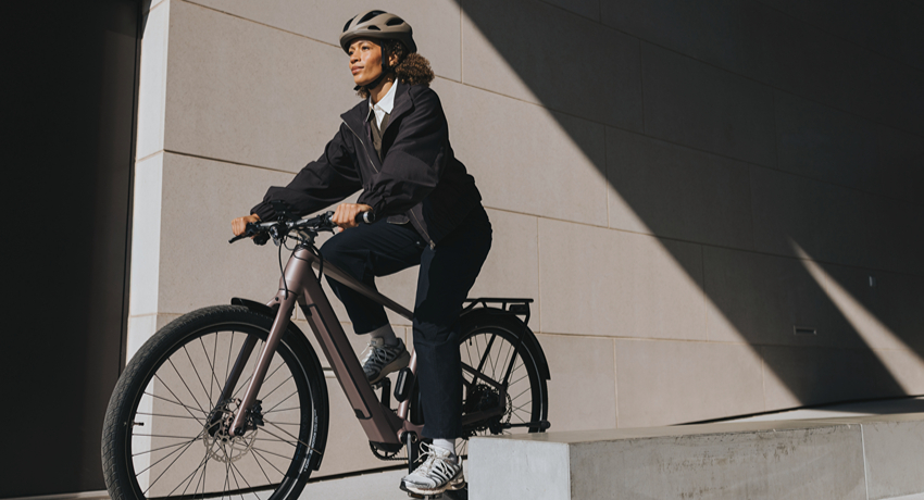 Une femme au guidon d'un VAE équipé du nouveau moteur roue arrière Bosch HubLine dans un environnement urbain minéral.